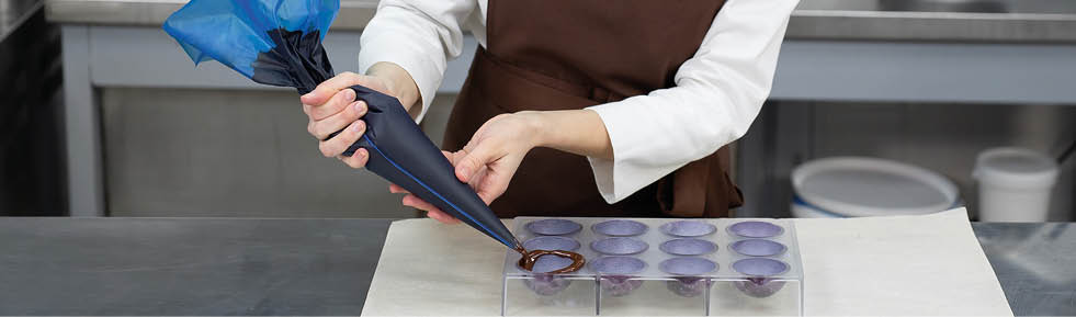 Chocolatier pours the chocolate into the molds. Pastry bag chef fills the hot melted chocolate into a silicone mold.