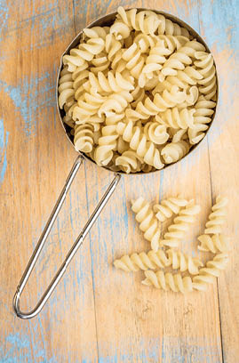 healthy, gluten free quinoa pasta (fusilli) - top view of a metal measuring cup against painted wood
