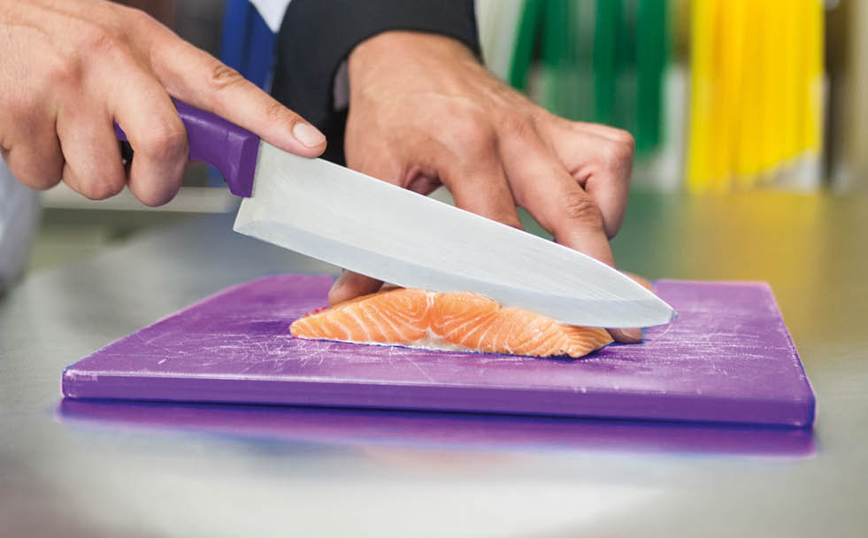 Chef slicing raw salmon with knife in professional kitchen