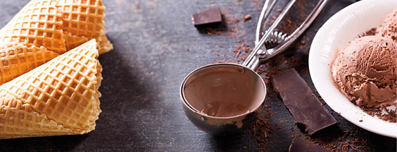 plate of chocolate ice cream scoops with pieces of chocolate bar and waffle cones on dark background, banner.
