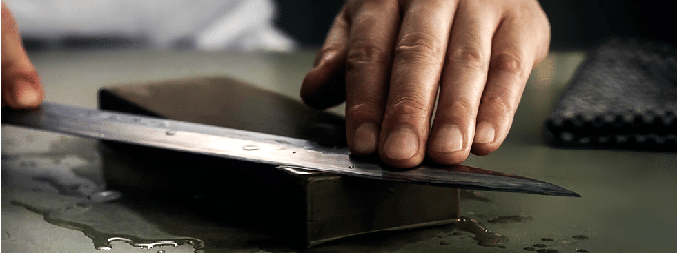 Great chef is sharpening the knife with whetstone