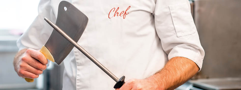 Portrait of chef cook in uniform with knifes at the restaurant kitchen