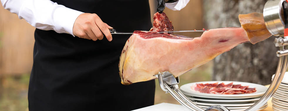 The chef is cutting the ham. image of a ham cutter with a knife cutting a thin slice of ham. Dried Ham, Serrano Ham, Acorn, Iberian, Italian or Parma Raw Prosciutto