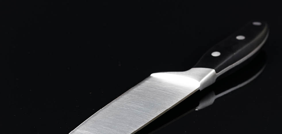 Chefs big kitchen knife isolated above black background with reflections.