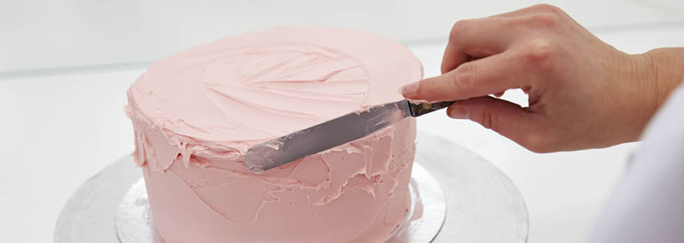 Close Up Of Woman In Bakery Decorating Cake With Icing