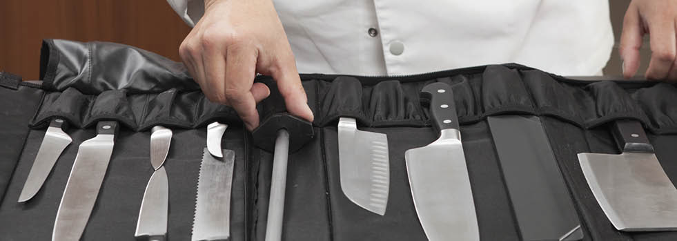Midsection of male chef selecting knife sharpener out of full set in commercial kitchen