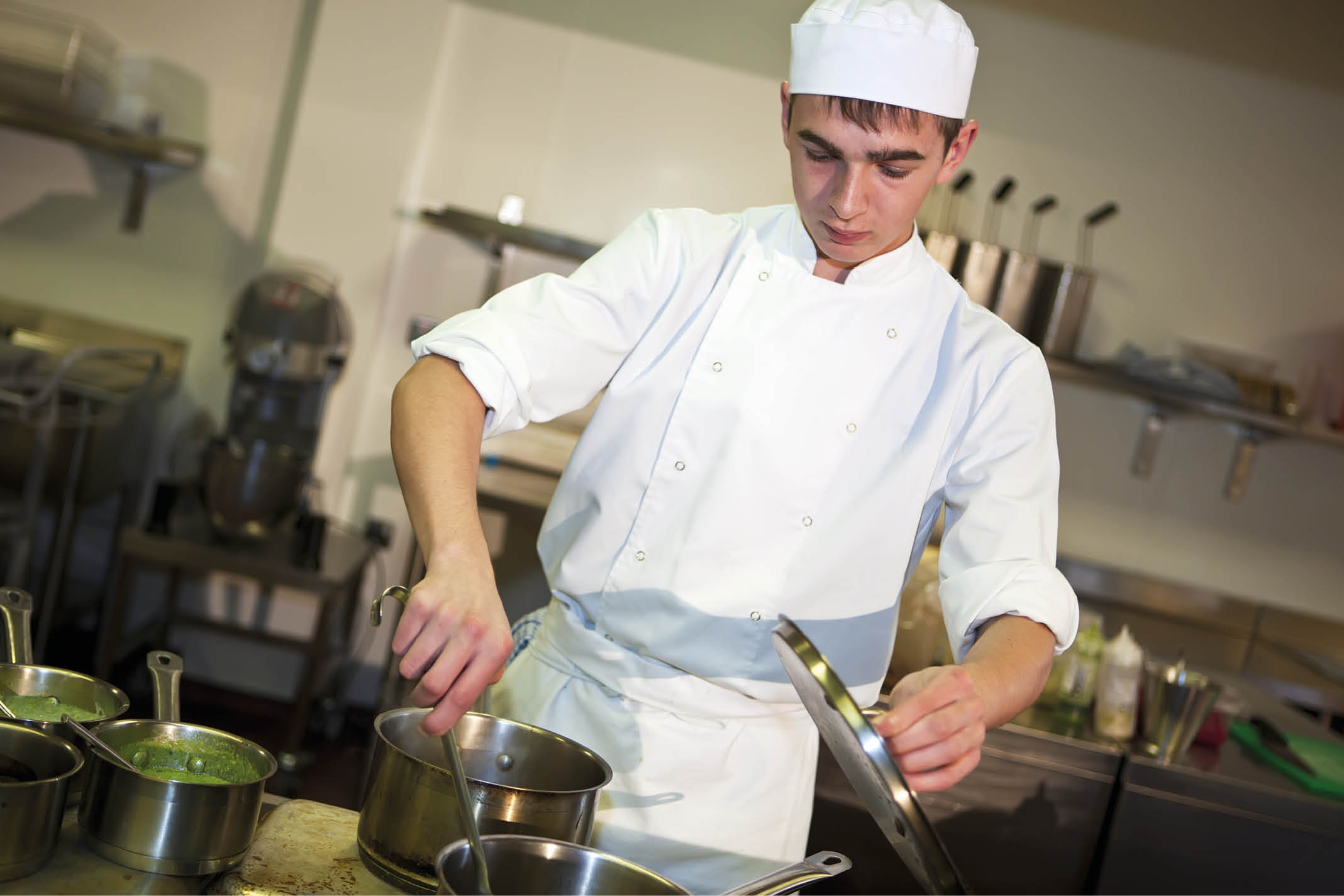 Young male chef cooking meal at the stove stirring food in a pan