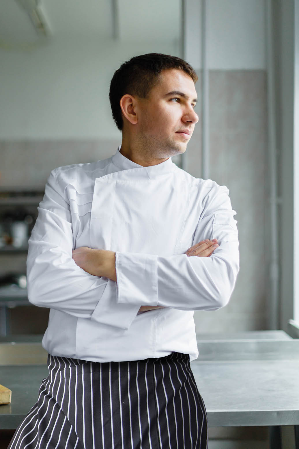 Young male chef posing with hands crossed at kitchen.
