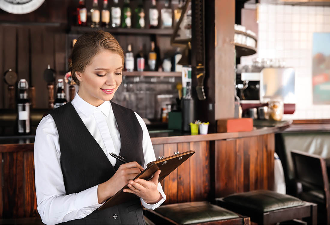 Young female waiter with clipboard in restaurant