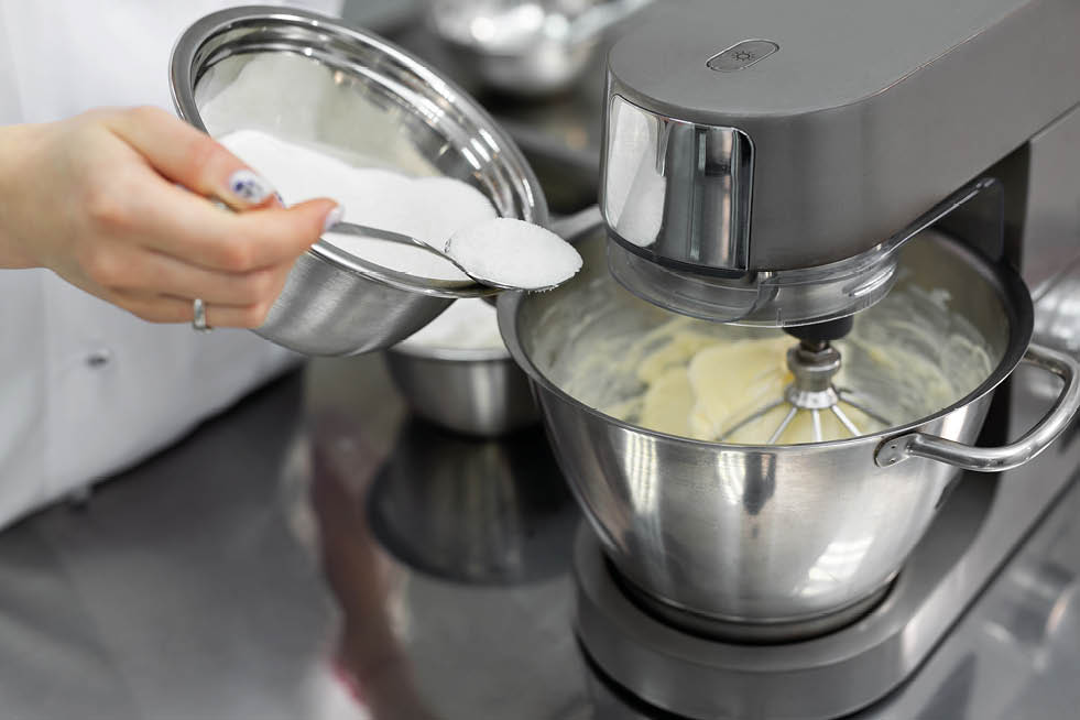 Pastry chef in the kitchen adds sugar to the kitchen machine, mixer.
