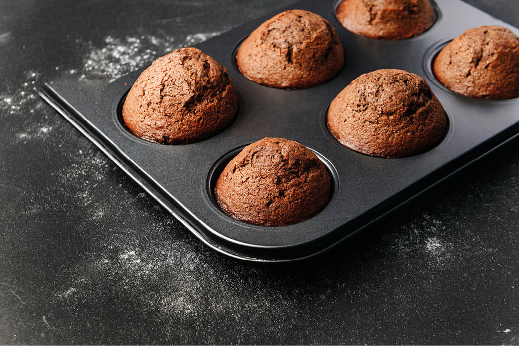 homemade muffins, in a baking dish on a dark surface, sprinkled with flour.