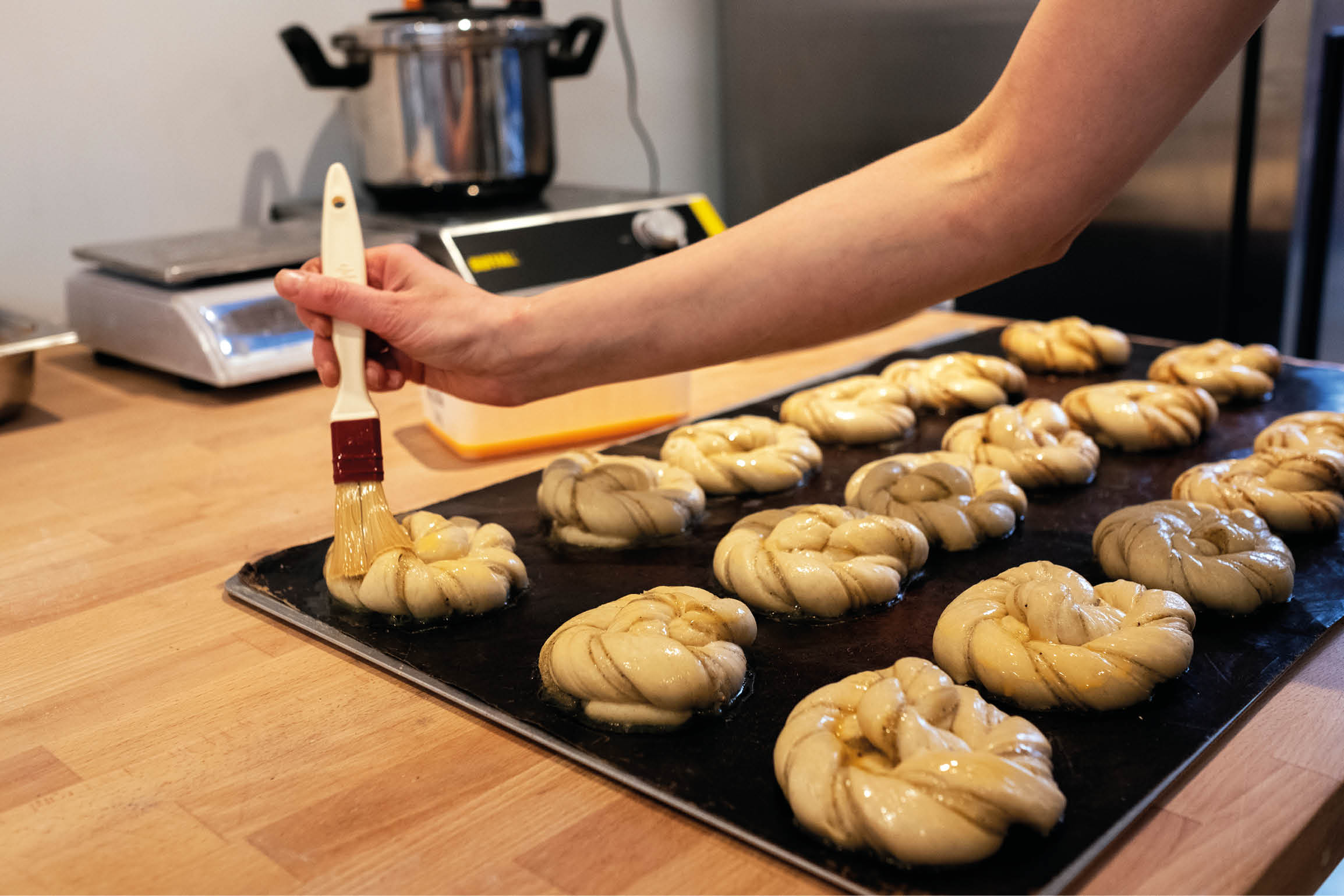 Close up person brushing cinnamon buns on a baking tray in an artisan bakery.