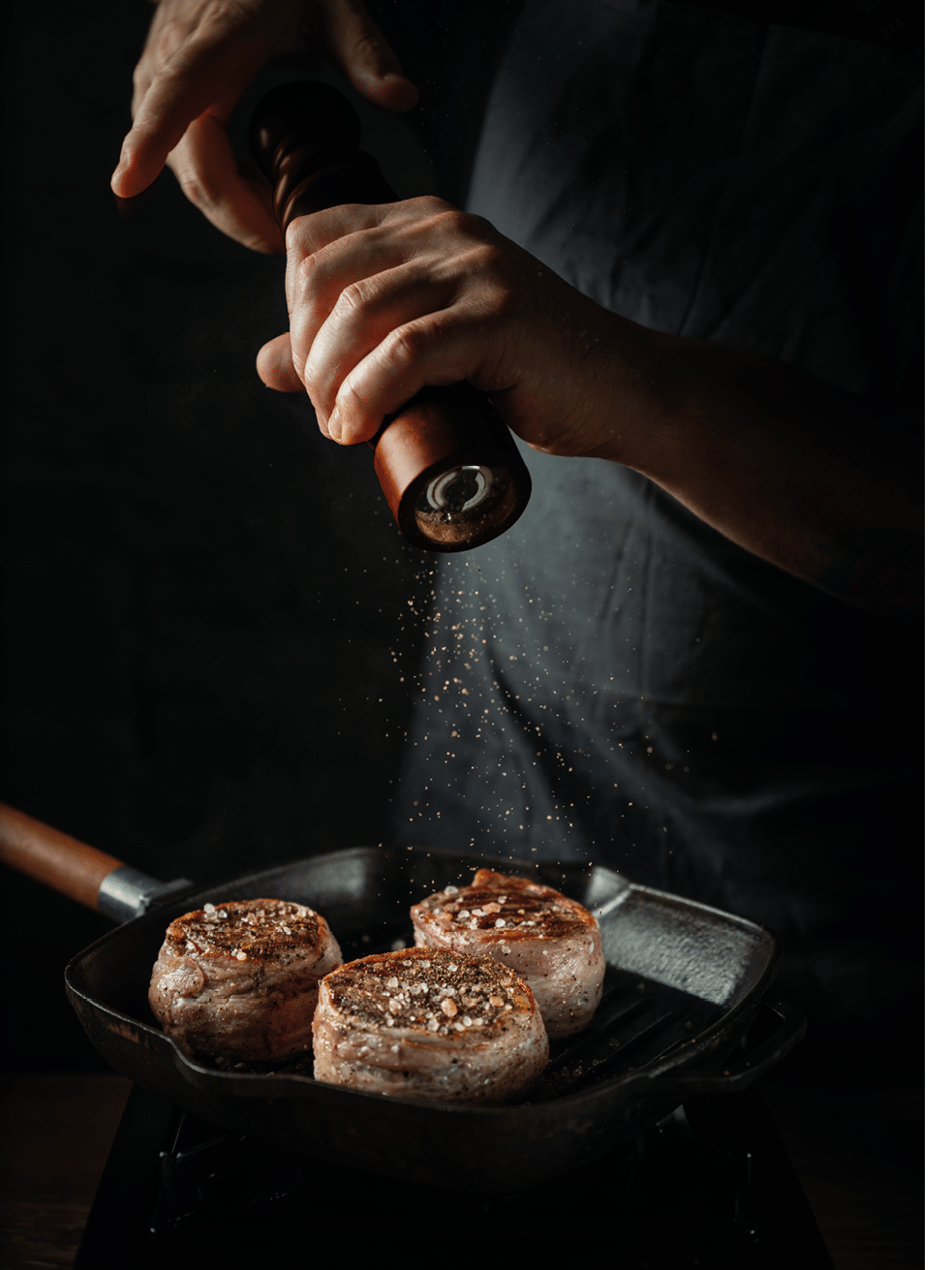 Close up chef hands adding pepper in mill during cooking beef steak on grill pan black background for copy space text restaurant menu,